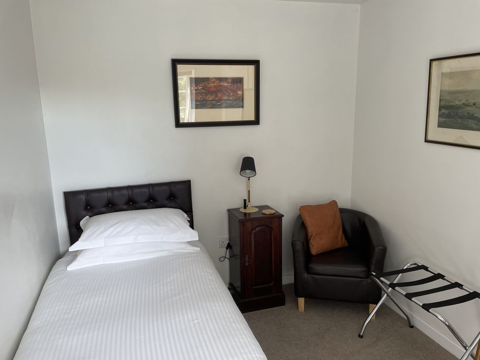 A bedroom with a bed, nightstand, lamp, and a chair at The Coach House in Bodmin