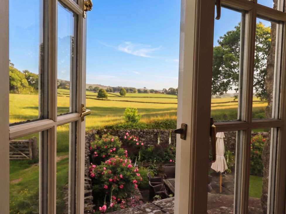 A view of a garden with flowers and a table from a window at The Garden Rooms Lawkland Austwick