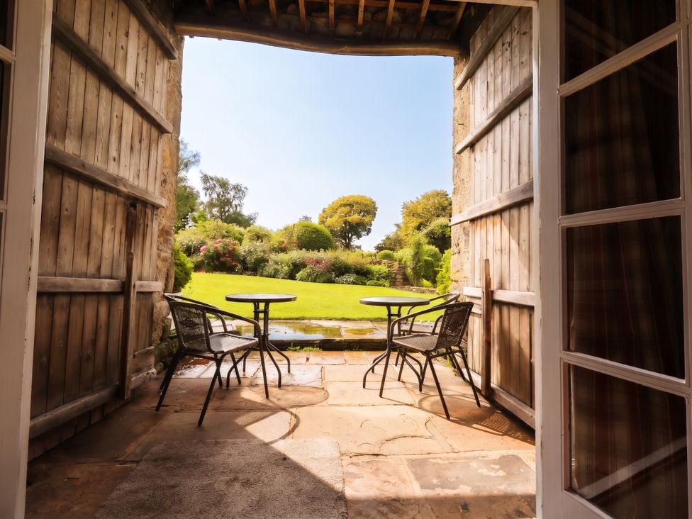 A view of a garden with a table and chairs from a doorway at The Garden Rooms Lawkland in Austwick