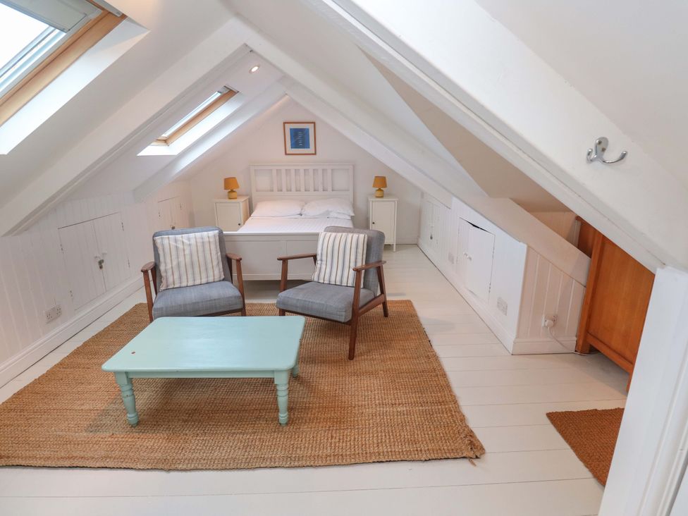 A loft with a bed, chairs, and a table at Badgers Loft in Sennen Cove