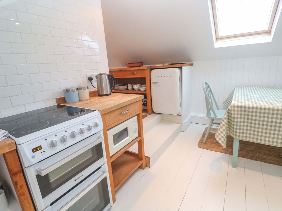 A kitchen with stove, fridge, and table at Badgers Loft Sennen Cove
