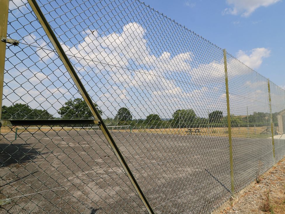 A chain link fence surrounding an open area with trees at The Cider Press, Motcombe
