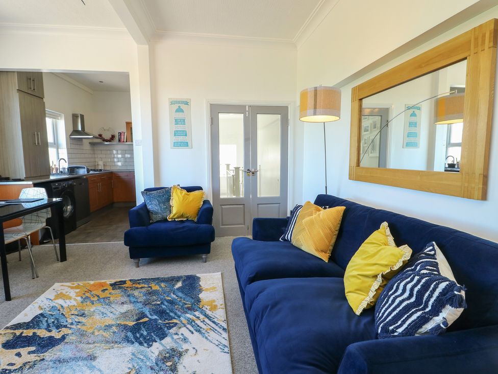 A living room with a blue sofa and open kitchen area at Little Orme View in Llandudno