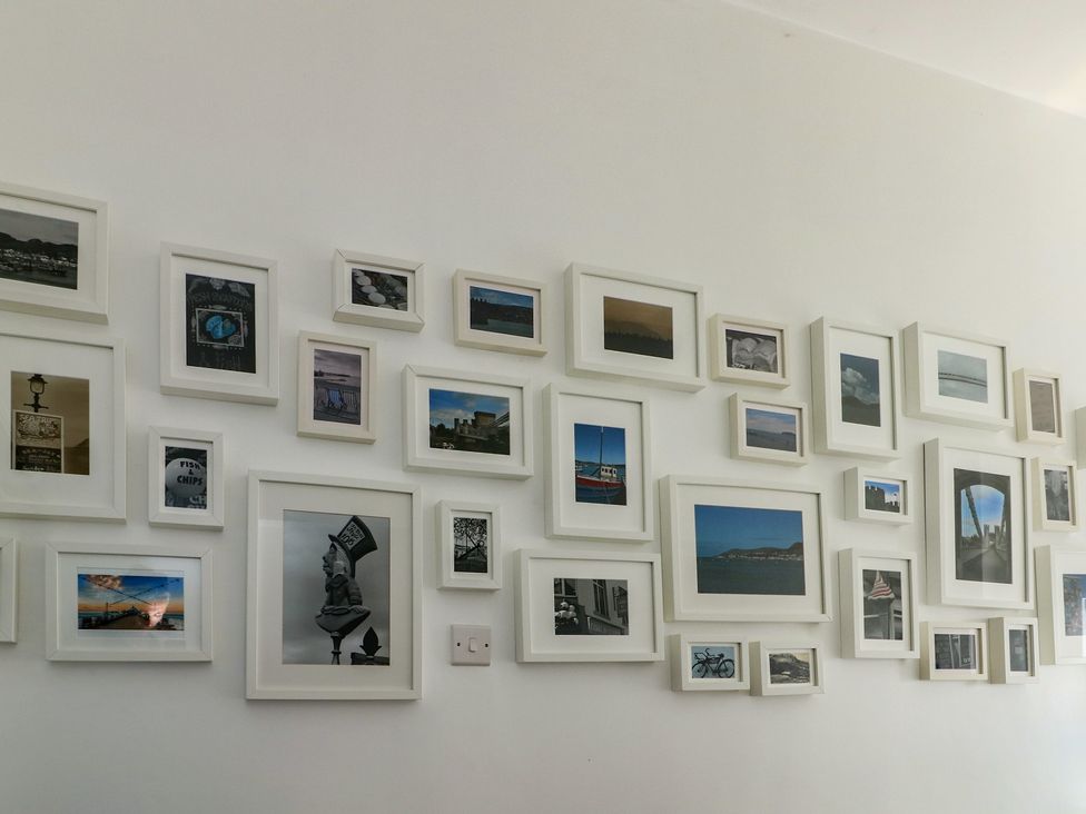 A wall with multiple photo frames in a living room at Little Orme View in Llandudno