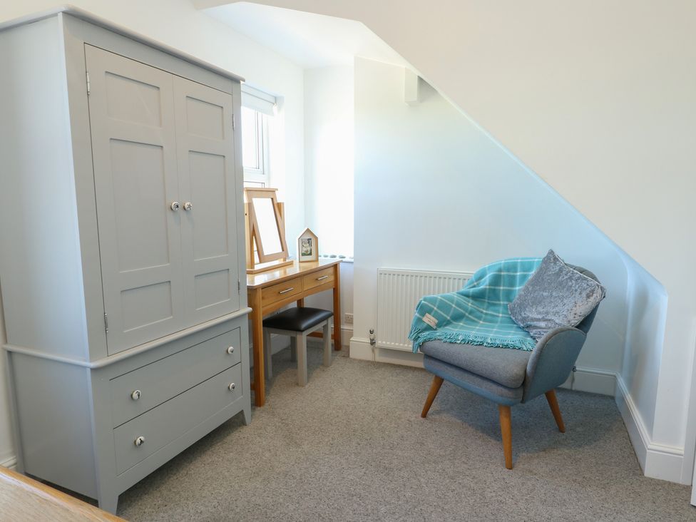 A bedroom with a wardrobe, chair, table and mirror at Little Orme View in Llandudno
