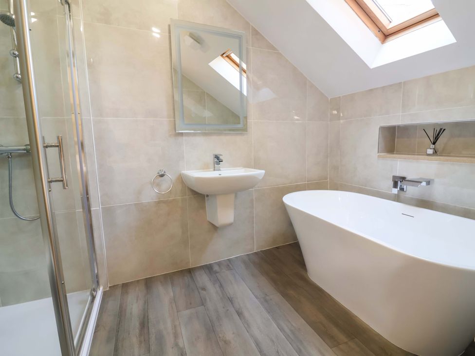 A bathroom with a shower, bathtub, sink, and mirror at The Linhay in Washford near Watchet