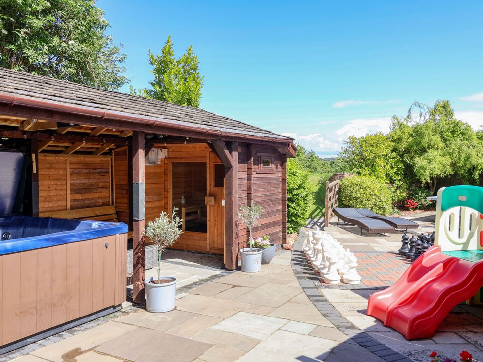 A hot tub and sauna in an outdoor area with a slide and deck chairs at The Linhay in Washford near Watchet