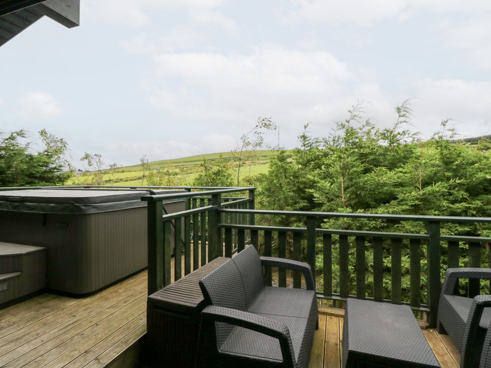 An outdoor deck with a hot tub and seating area at Elm Lodge in Ulverston