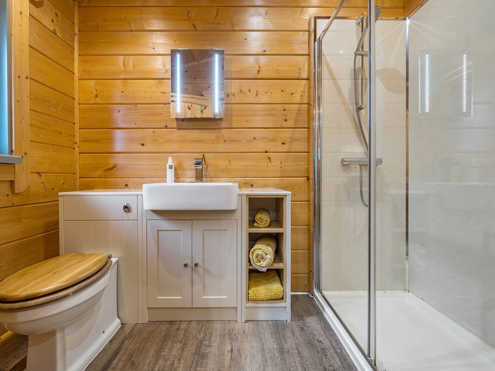 A bathroom with a shower, sink, and wood paneling at Elm Lodge in Ulverston