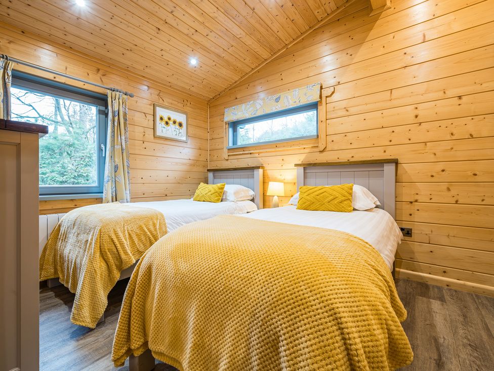 A bedroom with two beds, windows, and wooden walls at Elm Lodge in Ulverston