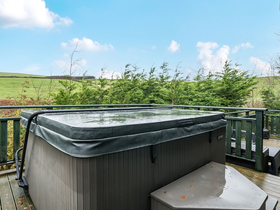 A hot tub on a deck surrounded by greenery at Elm Lodge in Ulverston
