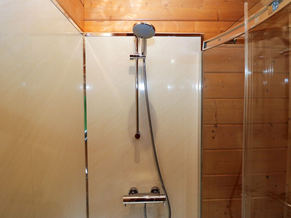 A shower with a wall and faucet at Elm Lodge in Ulverston