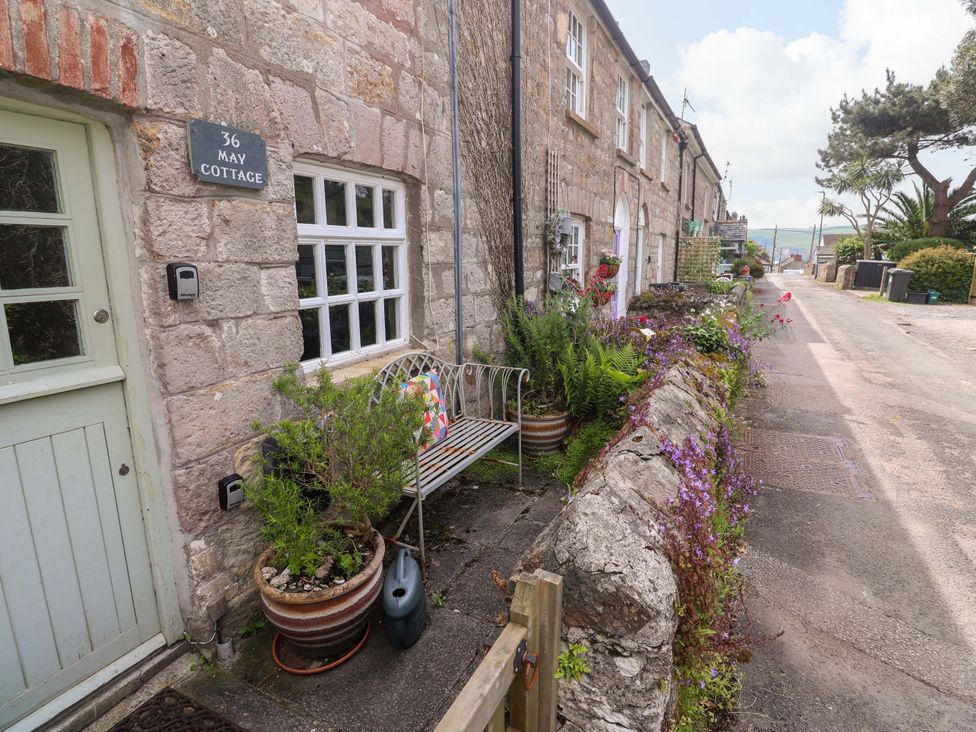 An outdoor view of May Cottage with a bench and flowers in Pentewan