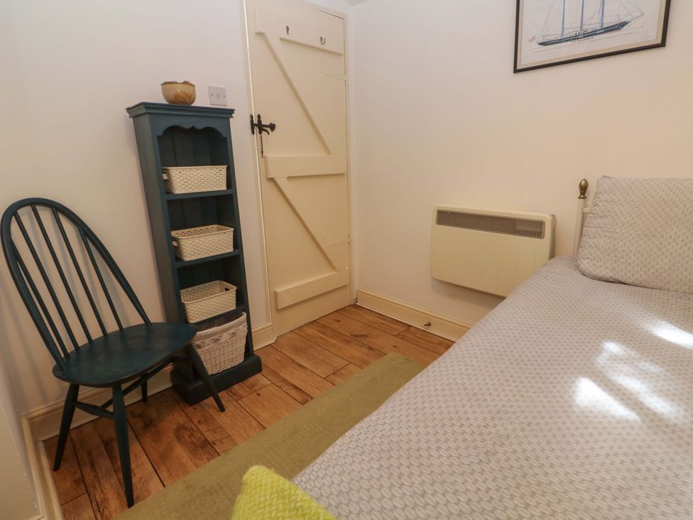 A bedroom with a bed, a chair, and a shelf at May Cottage in Pentewan