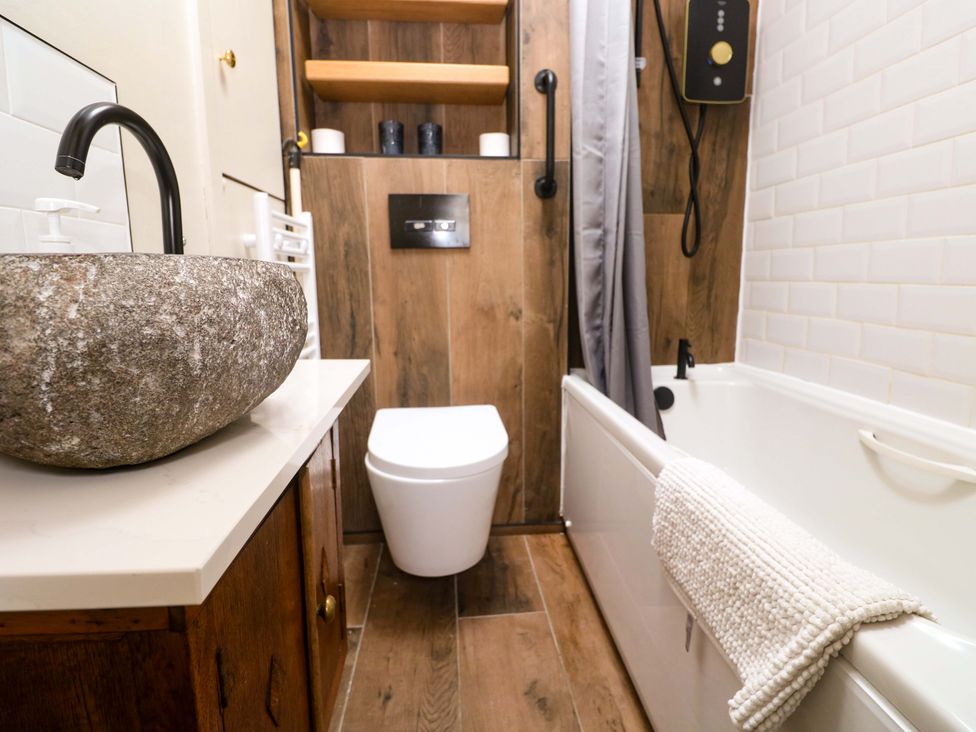A bathroom featuring a stone sink, toilet, bathtub, and wall-mounted shower at May Cottage in Pentewan