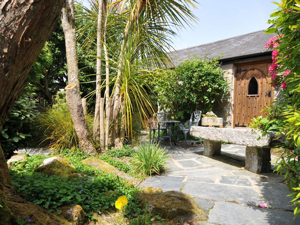 A garden with a stone bench and metal chairs at Trevenning Chapel Near Port Isaac