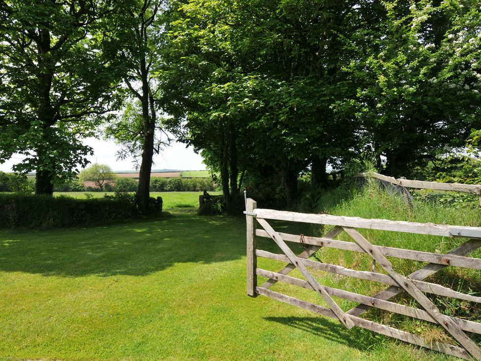 A garden with a wooden gate and trees at Trevenning Barn Near Port Isaac