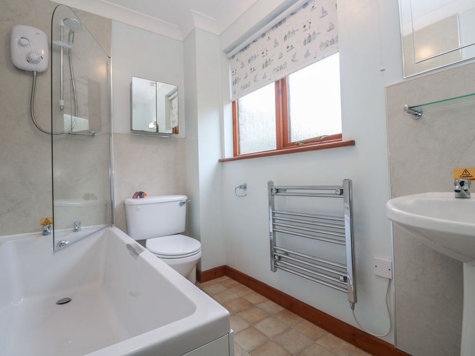 A bathroom with a bathtub, toilet, sink, and heated towel rail at Two Hoots in Falmouth