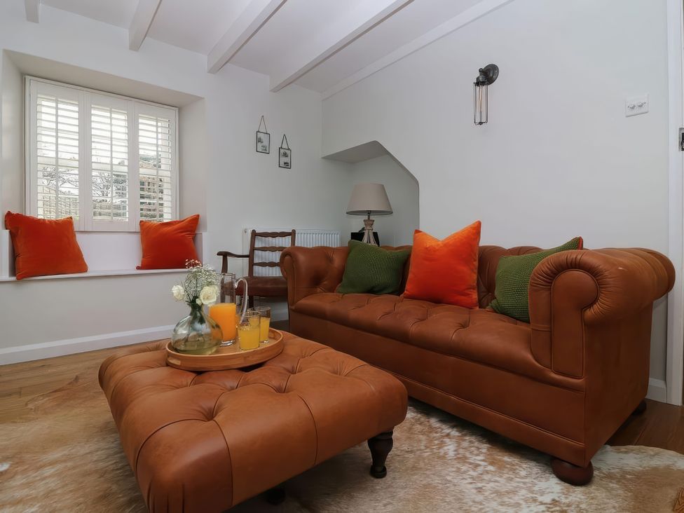 A living room with a leather couch and an ottoman at Trelan in Mevagissey