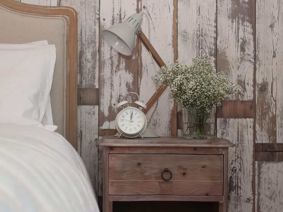 A bedroom with a lamp, alarm clock, and flowers on a nightstand at Trelan in Mevagissey