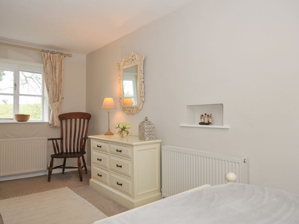 A bedroom with a dresser and chair at Stocks Barn in Looe
