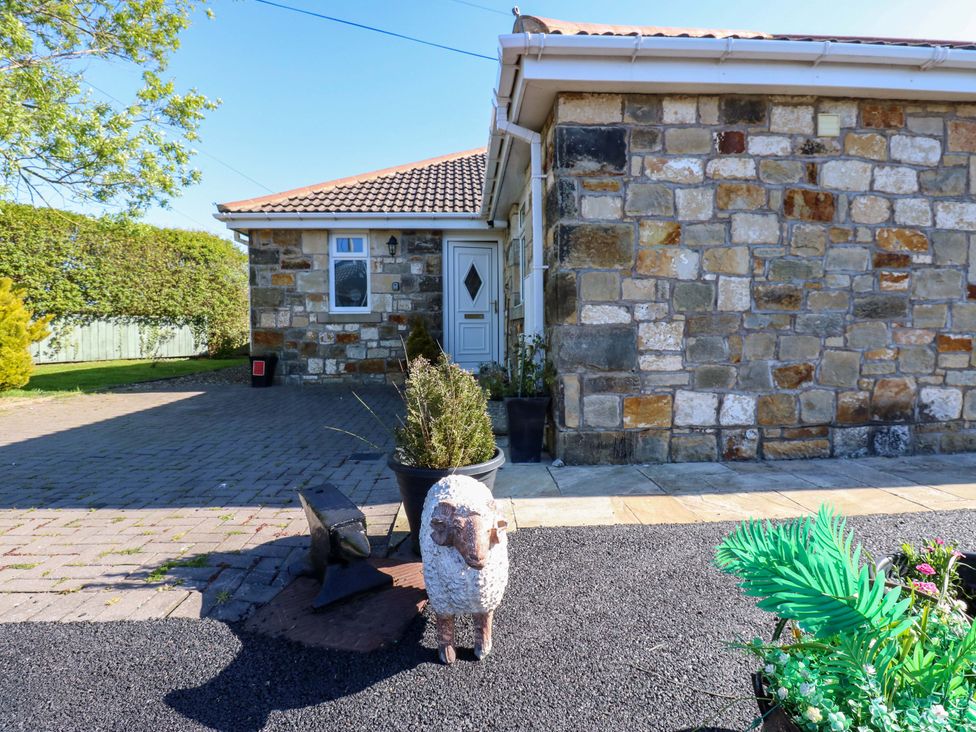 An outdoor area with a stone wall and sheep statue at Blacksmiths Cottage in Shilbottle