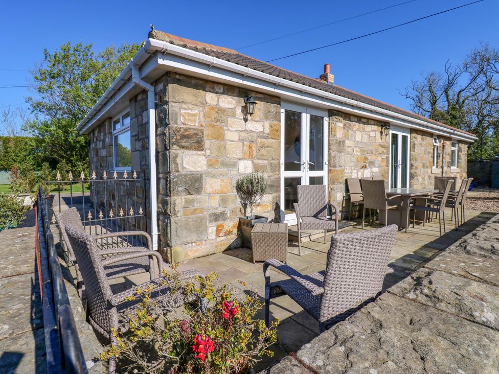 An outdoor area with stone wall, furniture, and plants at Blacksmiths Cottage in Shilbottle