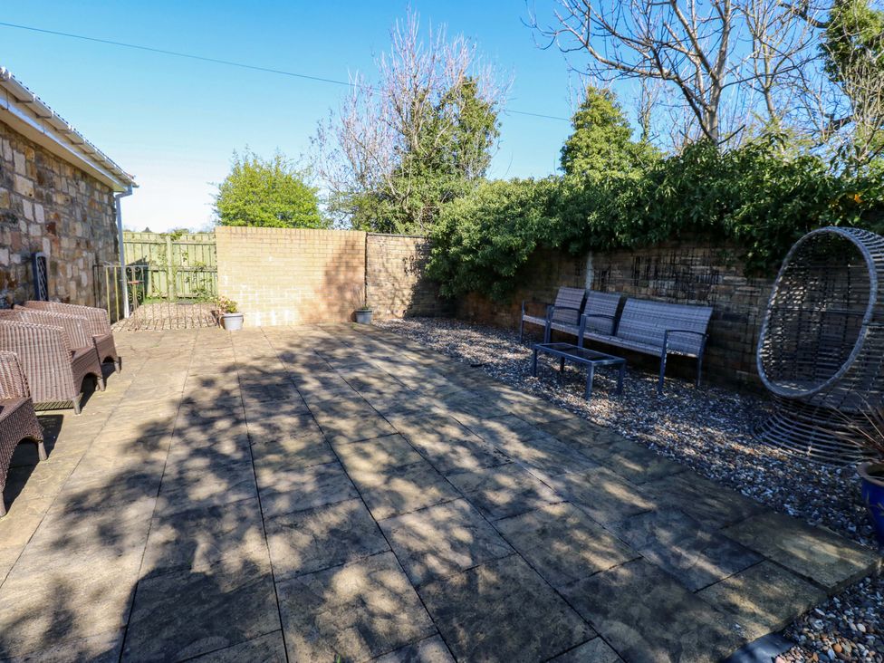 A garden patio area with seating and a wall at Blacksmiths Cottage in Shilbottle