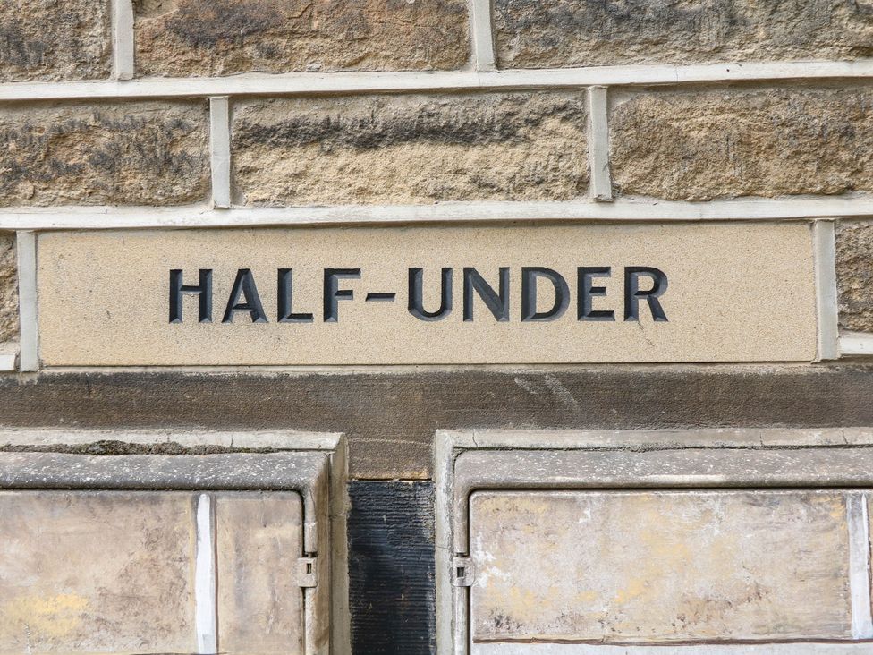 A sign displaying 'HALF-UNDER' mounted on a stone wall at Half Under