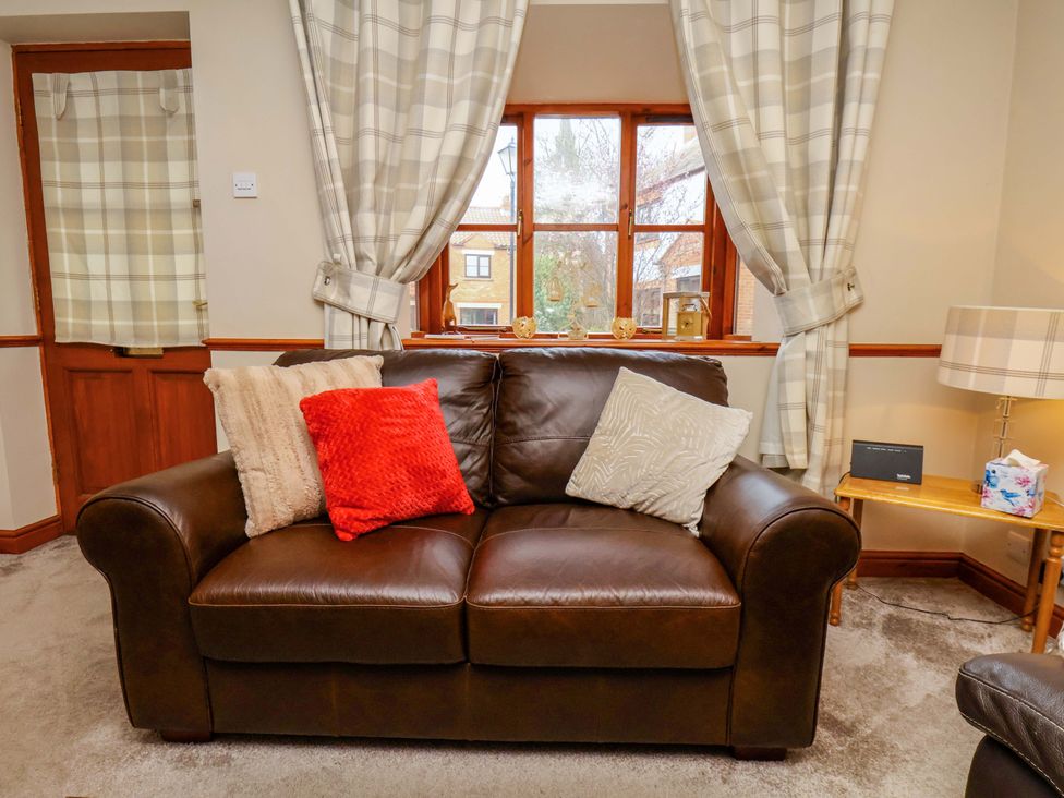 A living room with a brown sofa and cushions at Eskview Cottage in Ruswarp near Whitby