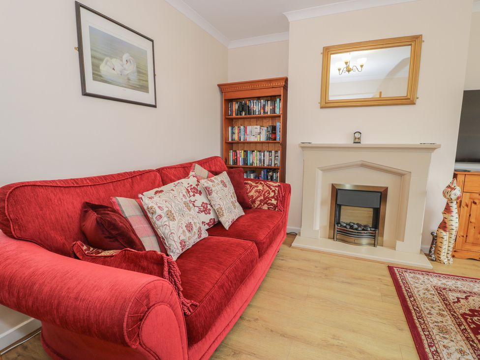 A living room with a red sofa and bookshelf at Bay View in Benllech