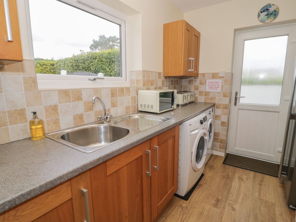 A kitchen with a sink, washing machine, and microwave at Bay View in Benllech