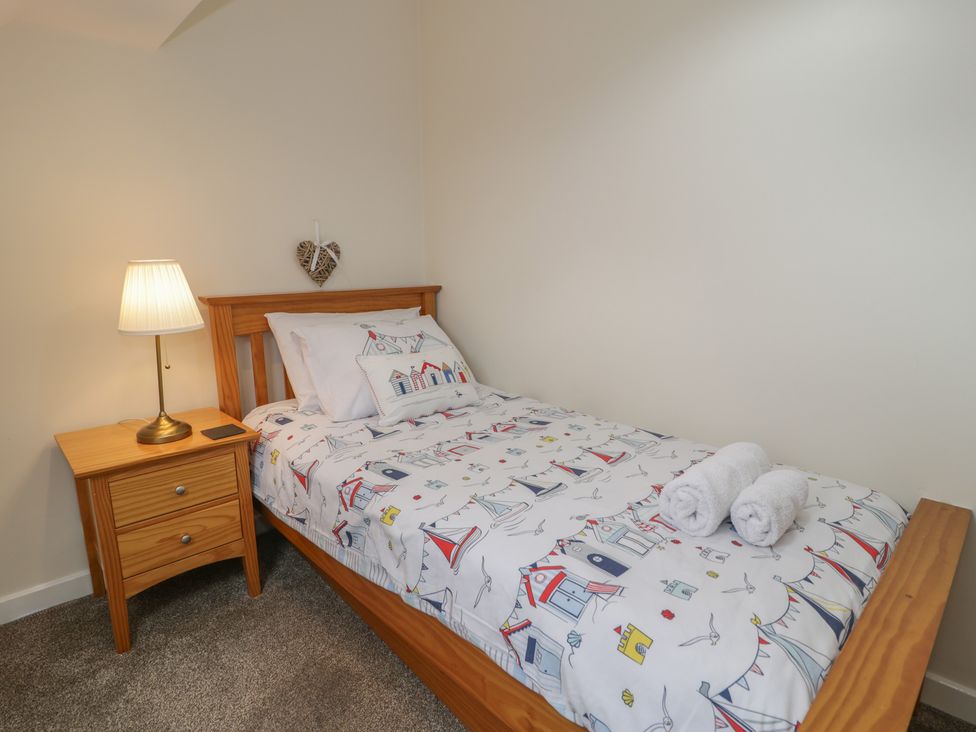 A bedroom with a bed, nightstand, lamp, and towels at Bay View in Benllech