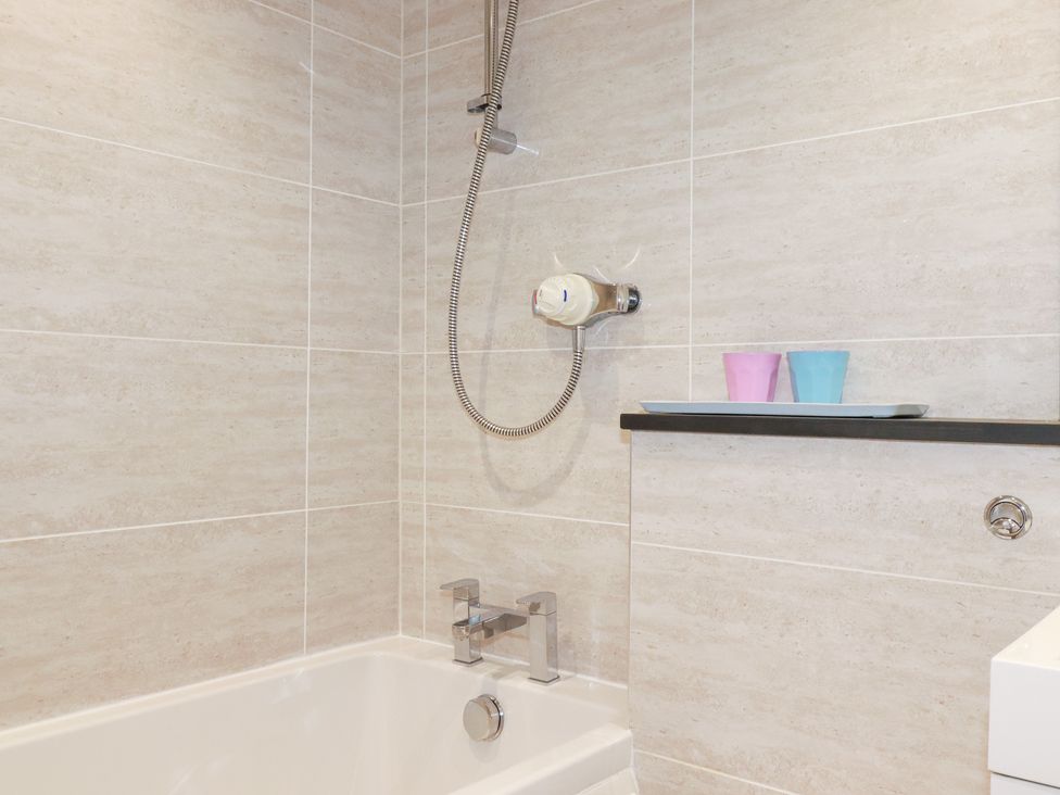 A bathtub with shower attachment and cups on a shelf at Gull Cottage in Padstow