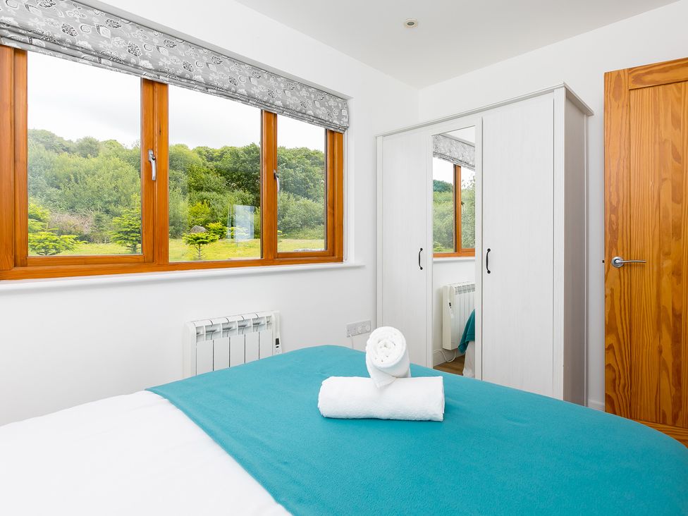 A bedroom with a bed, wardrobe, and windows at Tressa, Tor Down Quarry St Breward