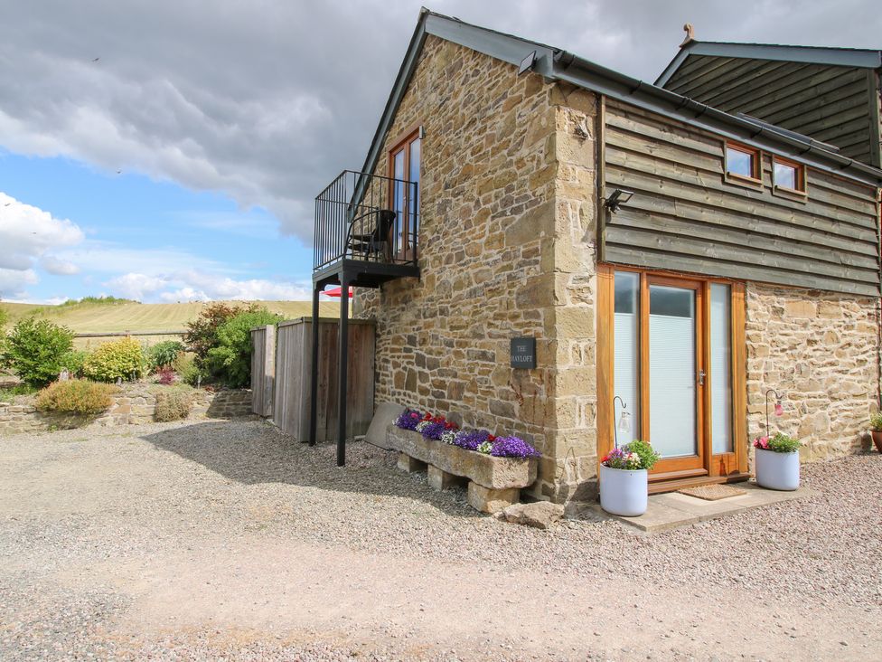 An outdoor view of a stone house with a balcony and garden at The Hay Loft Craven Arms