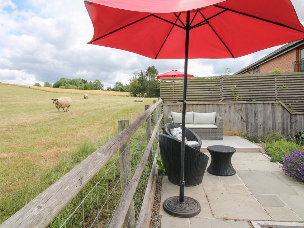 An outdoor seating area with an umbrella and sheep grazing at The Hay Loft in Craven Arms
