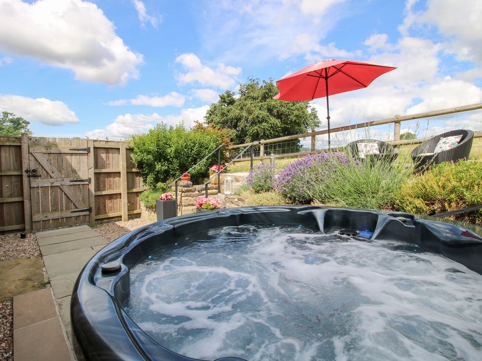 A hot tub with a garden setting and chairs at The Hay Loft in Craven Arms