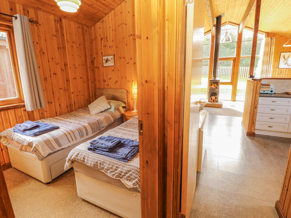 A bedroom with two beds and a view into the kitchen area at 26 Dukes Meadow in Greystoke near Penrith