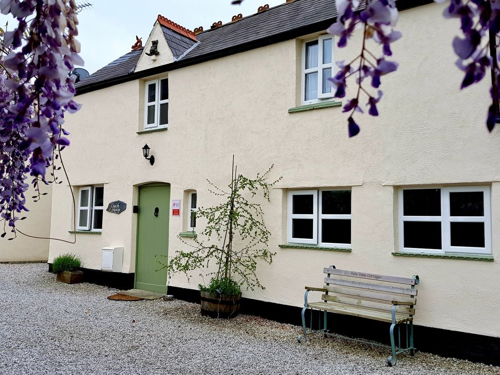 An exterior view of a cottage with a bench and plant at The Coach House in Prestatyn