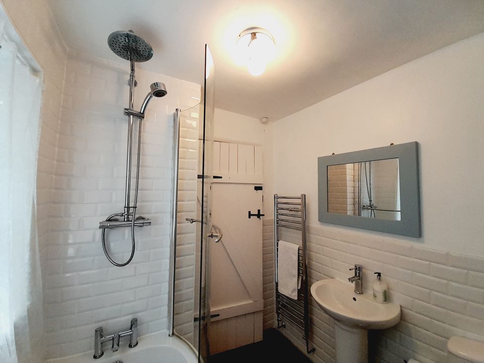 A bathroom with a shower, bathtub, sink, and mirror at Crab Cottage in Ilfracombe