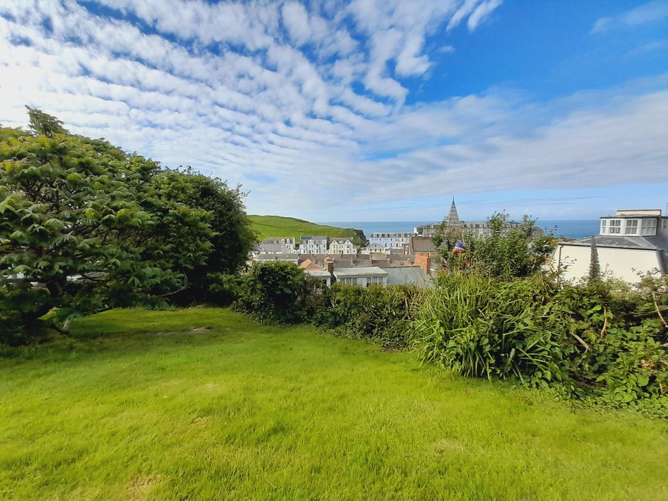 A garden with grass and bushes overlooking buildings and ocean at Crab Cottage Ilfracombe