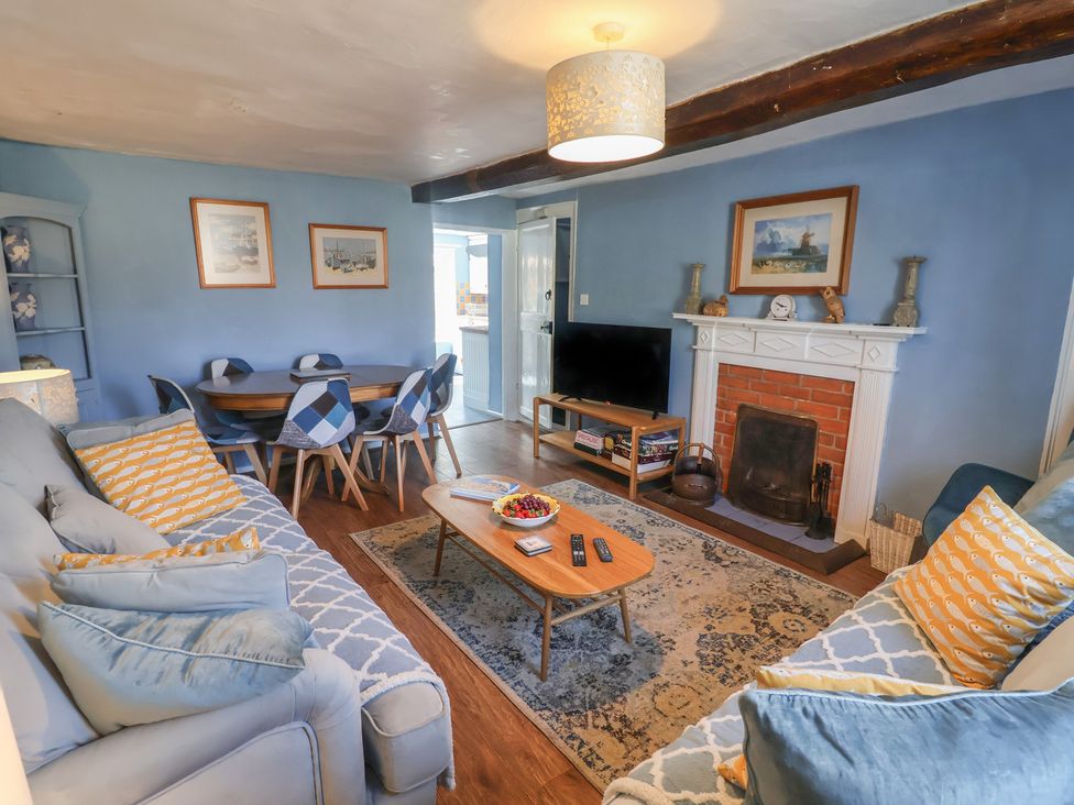 A living room with a sofa, dining table and television at Delphinium in Blakeney, Norfolk