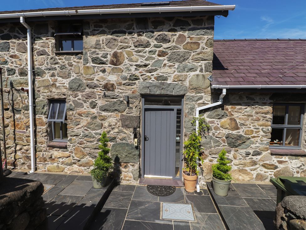 An outdoor area with stone wall, door, and planters at Wern Olau Cottage in Groeslon near Caernarfon