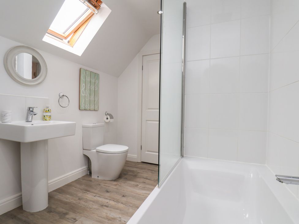 A bathroom with a tub, sink, toilet, and mirror at Coastal Cottage The Bay near Filey