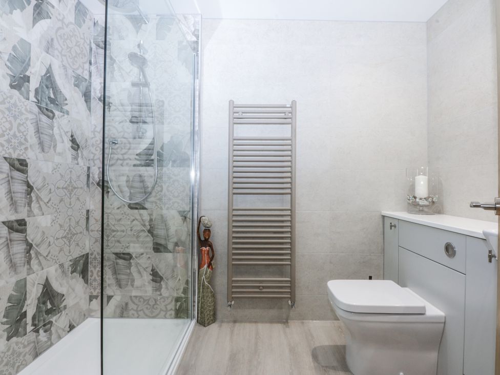 A bathroom with a shower, toilet, towel radiator, and vanity unit at 40 New Row in Pwllheli