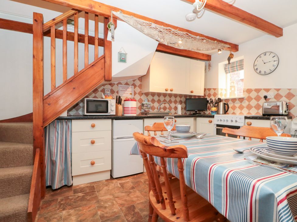 A kitchen with a dining table and wooden stairs at The Old Cottage in Staithes