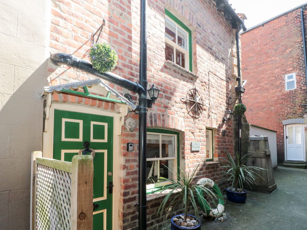 A brick exterior of a cottage with a green door and plants at The Old Cottage in Staithes
