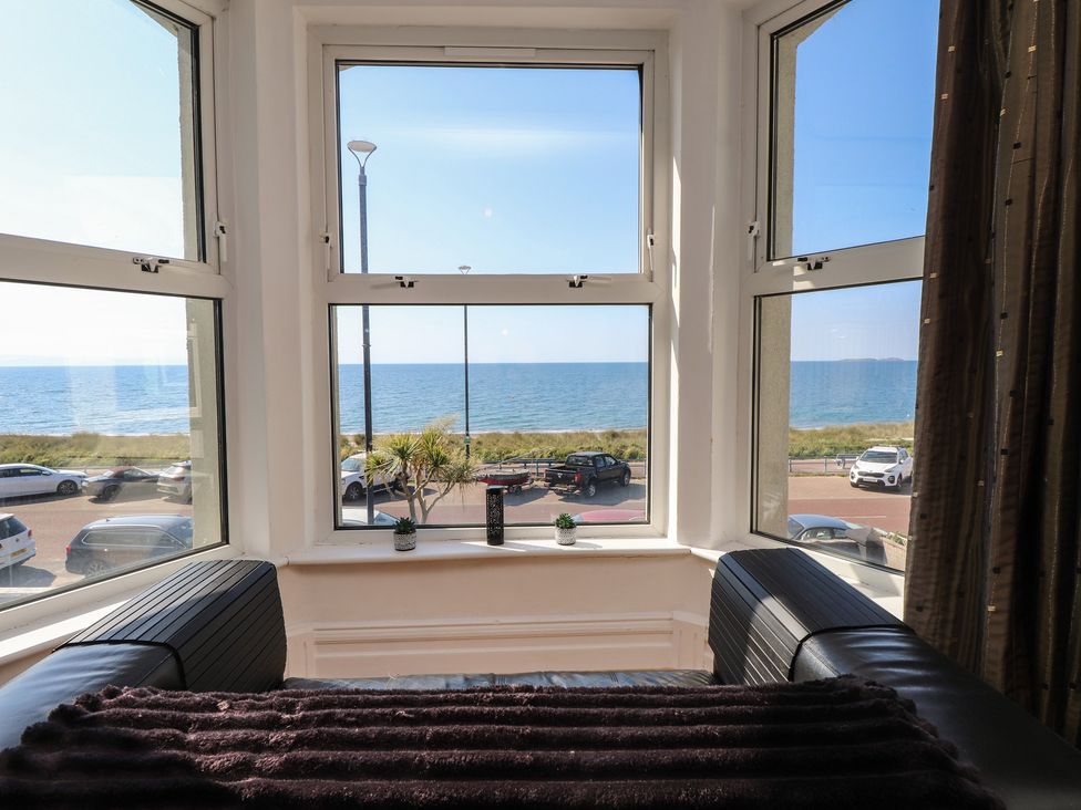 A living room with a view of the sea and parked cars at Wavecrest in Pwllheli