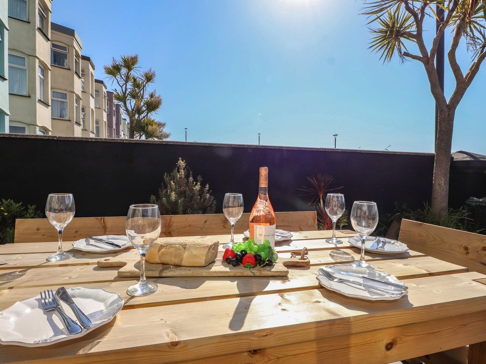 An outdoor dining area with a table, glasses, a bottle, and fruit at Wavecrest in Pwllheli